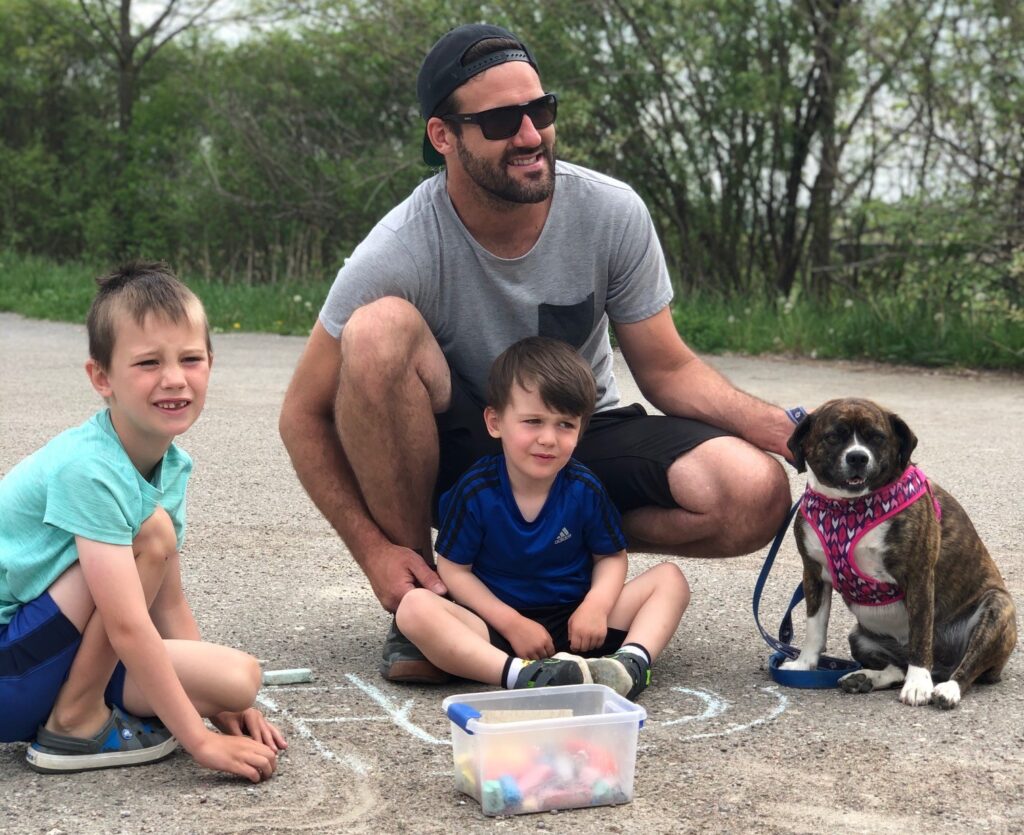man with two kids and dog painting chalk on pavement