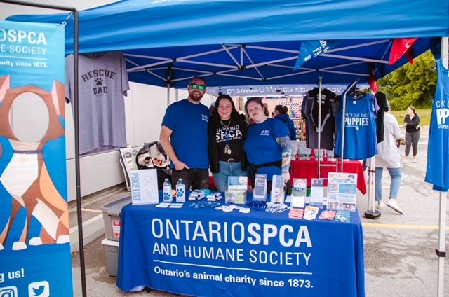 Ontario SPCA and Humane Society booth with three people in blue shirts standing behind a display table at an outdoor event