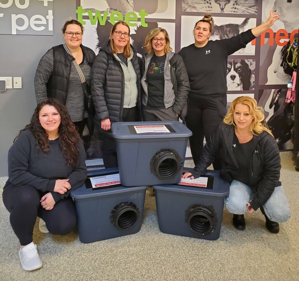 Group of six people posing with assembled outdoor cat shelters inside an animal centre