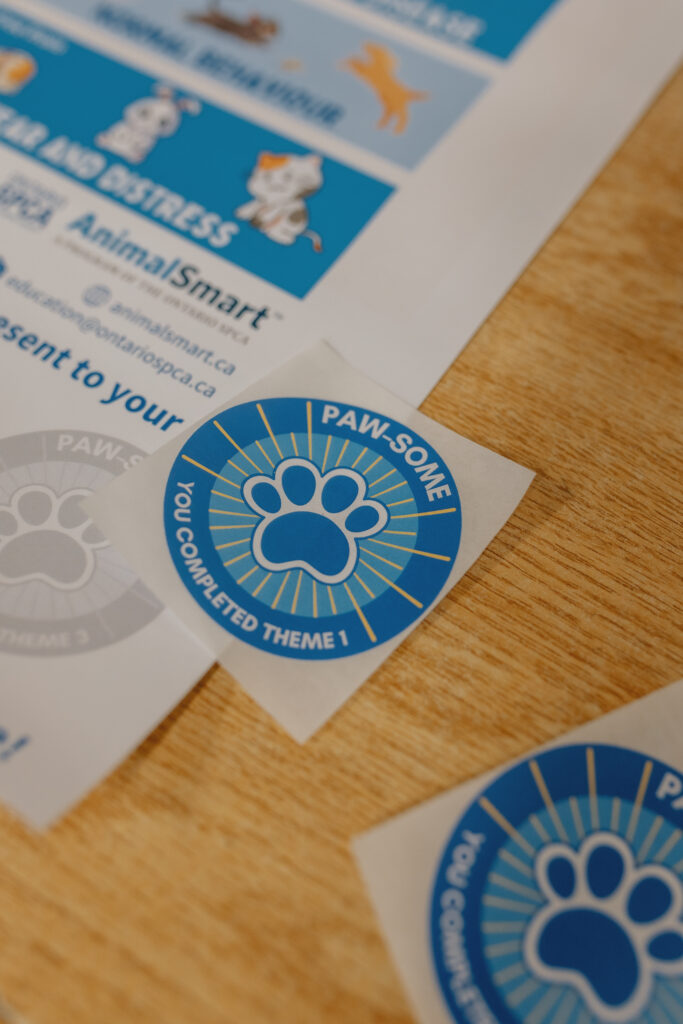 AnimalSmart™ PAW-SOME sticker reading 'You Completed Theme 1' placed on a wooden table beside program materials