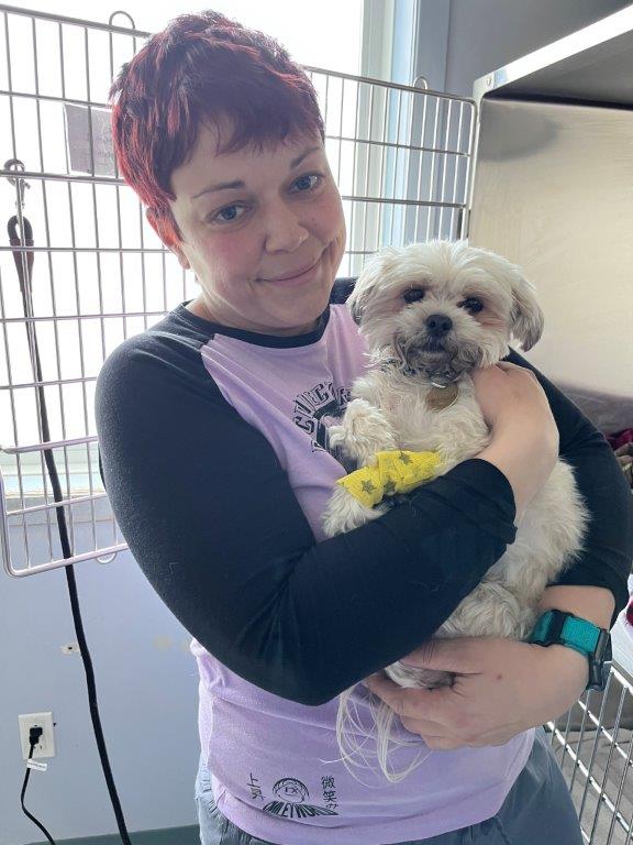 Woman holding small tan dog in her arms, with an open cage door behind her, both looking at the camera and appearing content.