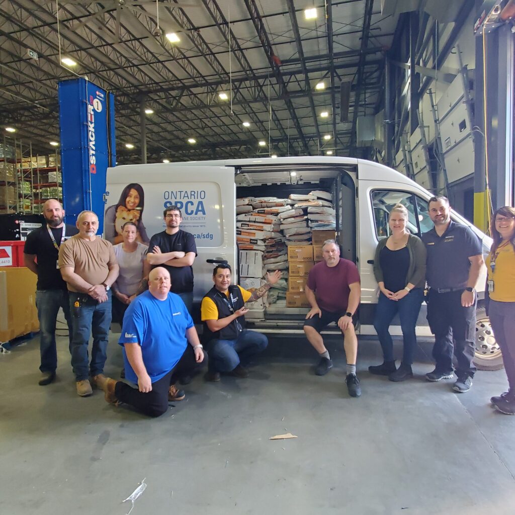 Group of Ontario SPCA and Humane Society staff and partners posing in a warehouse beside a van loaded with stacked bags and boxes of pet food.