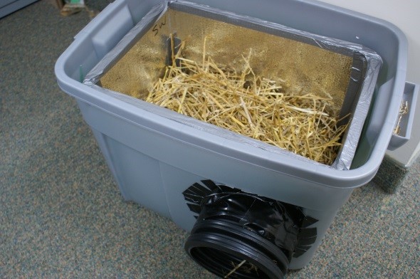 Plastic storage bin converted into an outdoor cat shelter with straw bedding and a circular entrance