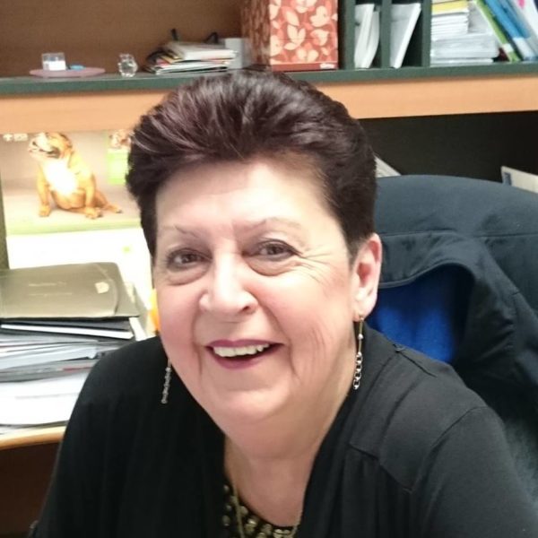 Liz smiling at her desk in an office setting, with papers and a dog calendar in the background.