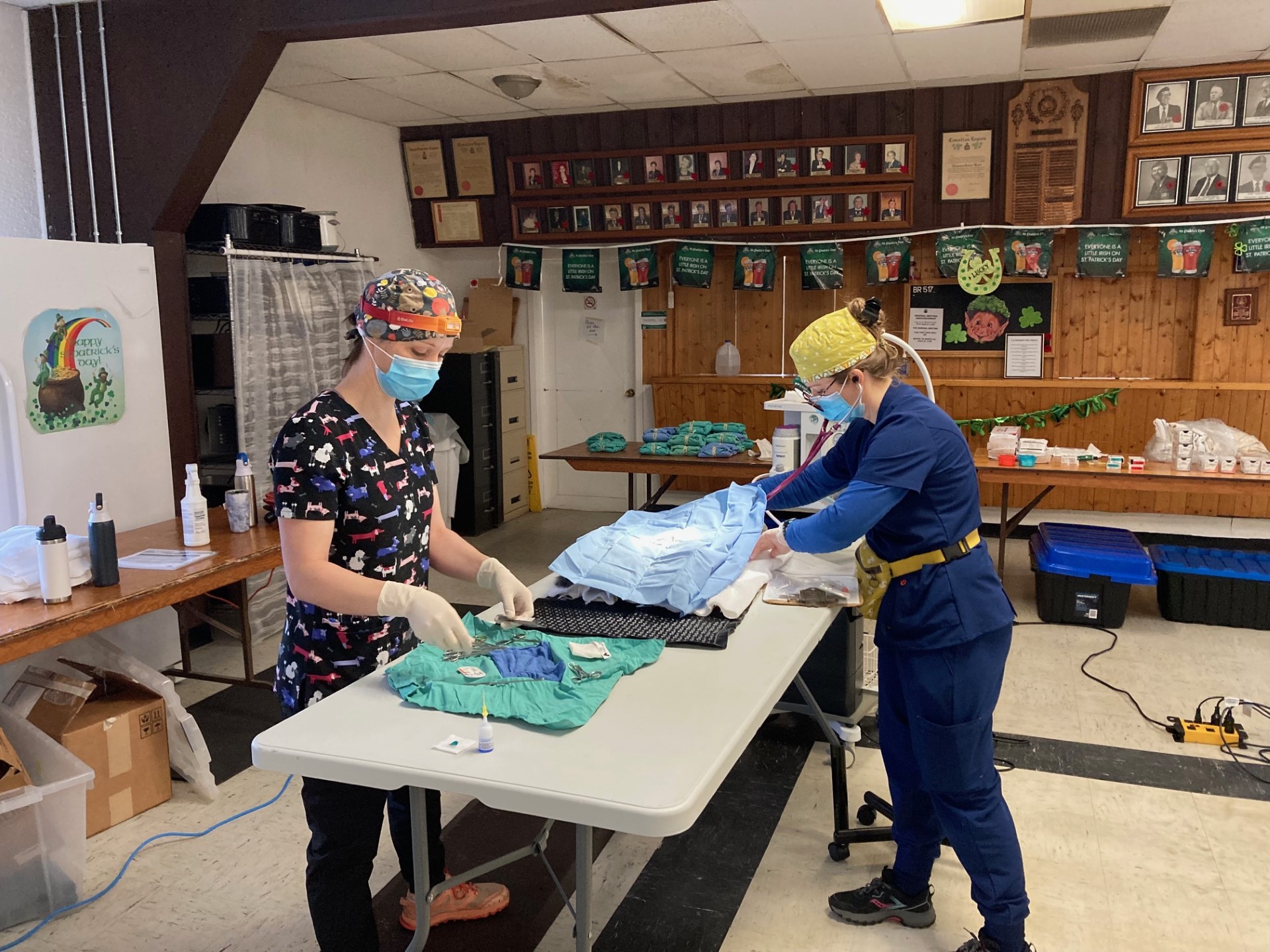 Two veterinary professionals wearing masks and scrubs preparing surgical supplies at a community spay and neuter clinic.