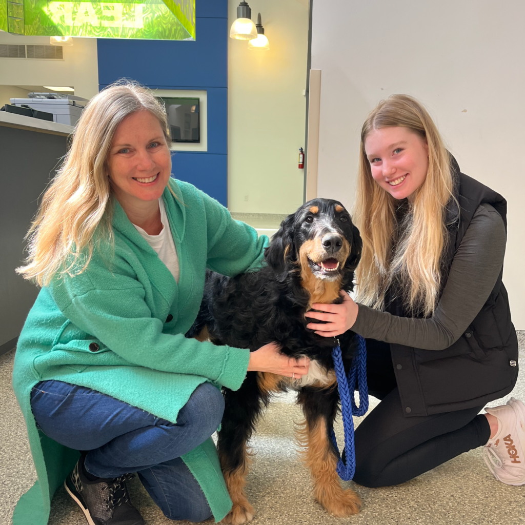 Two women crouching down and posing on either side of a happy looking dog.