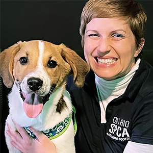 Ontario SPCA team member smiling while holding a happy dog wearing a patterned green collar.