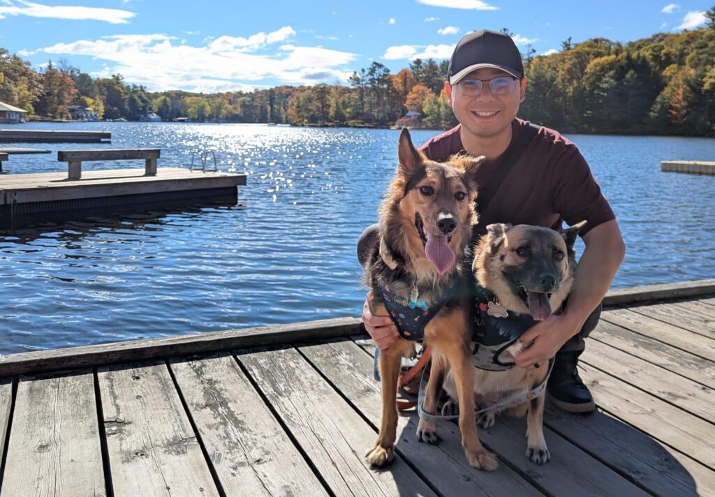 Man on dock with two dogs smiling at camera.