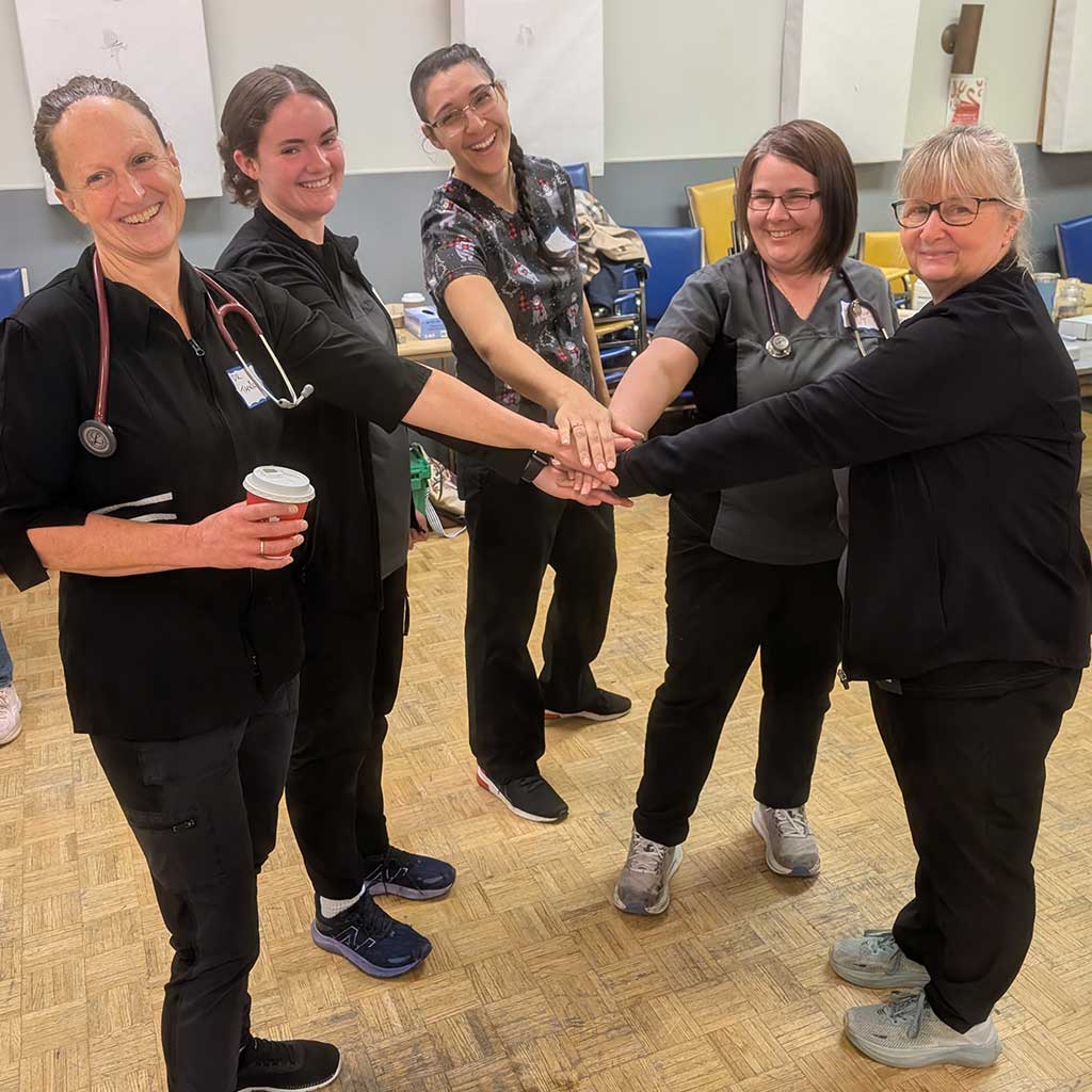 Veterinary clinic team members standing together indoors with hands stacked, smiling and showing teamwork