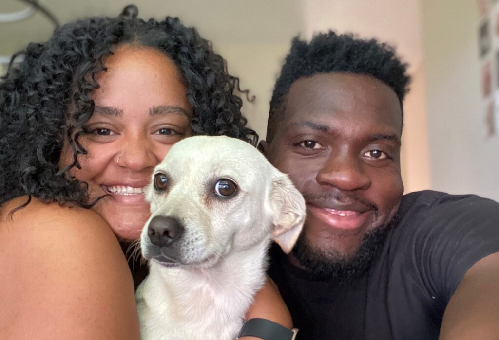 **15.** Smiling couple posing with their small white dog, gathered closely together for a family photo at home.