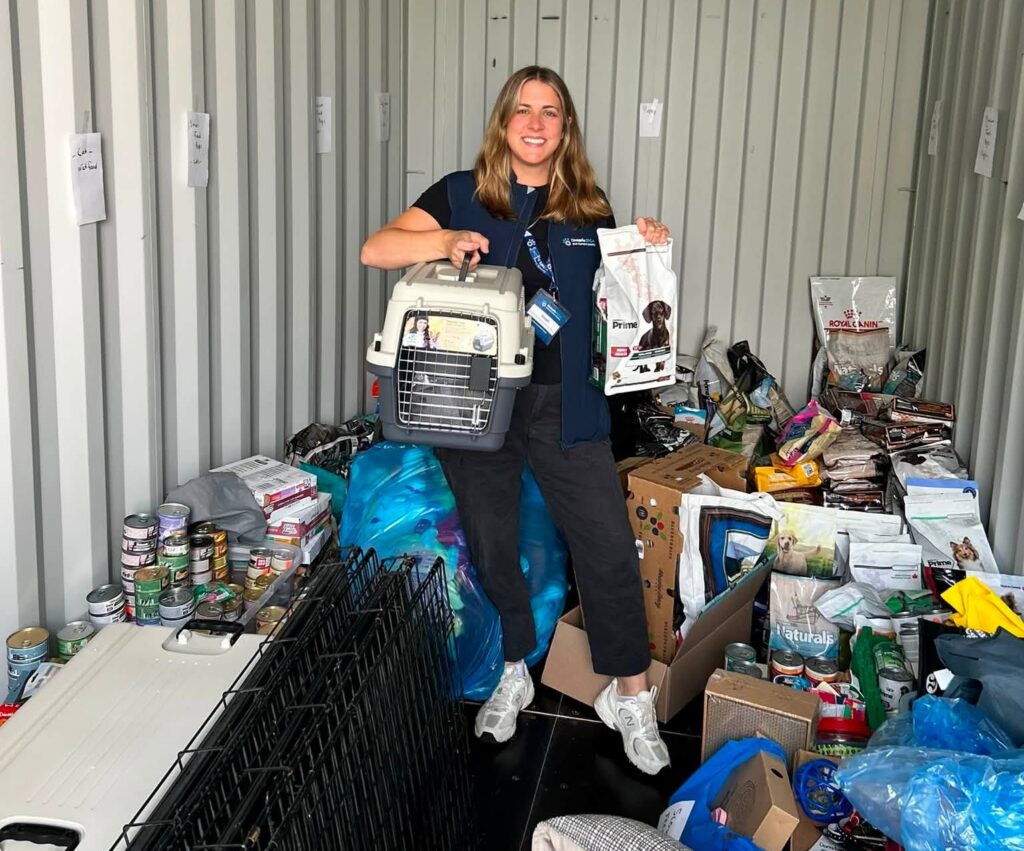 An Ontario SPCA team member stands inside a storage container filled with donated pet supplies, holding a pet carrier and a bag of dog food.