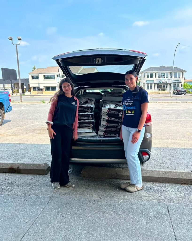 Two volunteers stand beside an SUV filled with donated pet food and supplies ready to support wildfire evacuees and their animals.