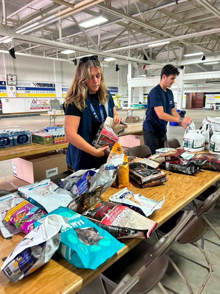 Ontario SPCA team members sort donated pet food and supplies on tables inside an emergency response centre for wildfire evacuees.