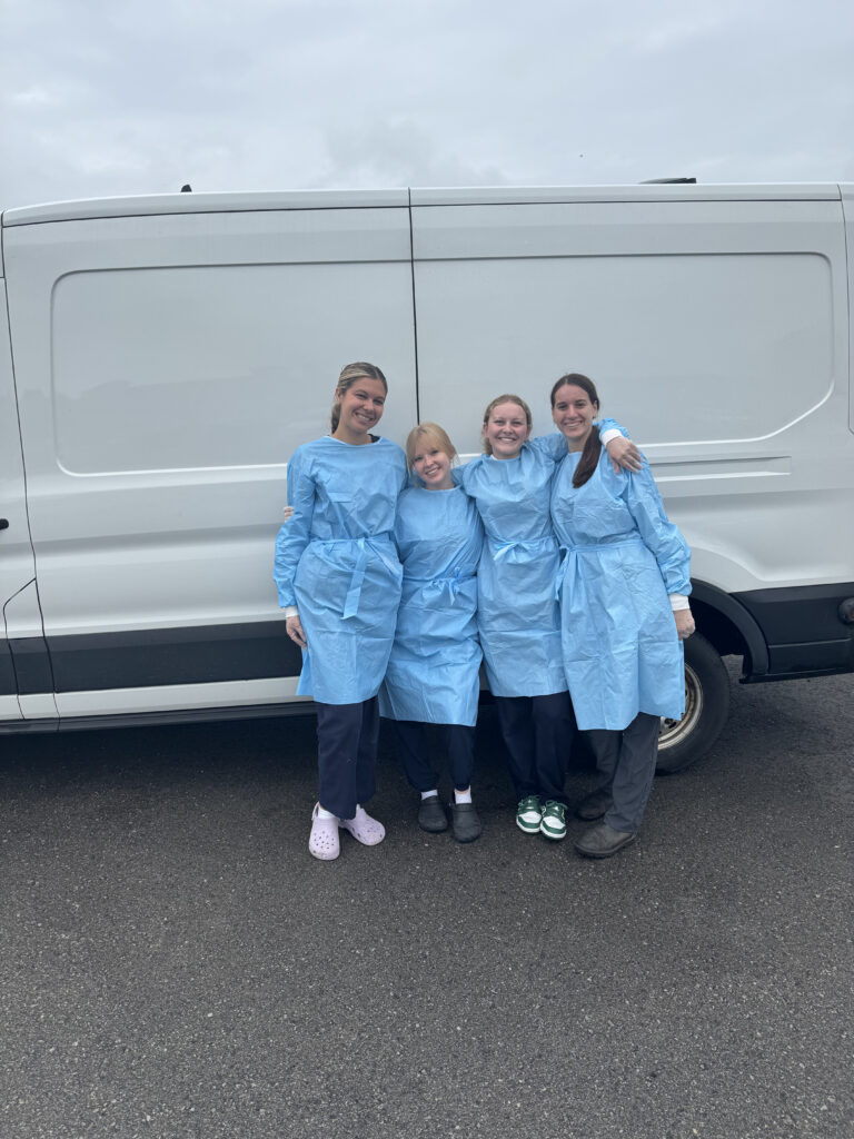 Four female volunteers in blue protective gowns posing together in front of white Ontario SPCA mobile unit