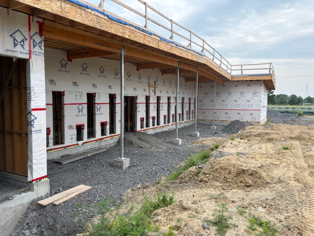 Construction site exterior showing house wrap membrane, window openings, and completed structural framing