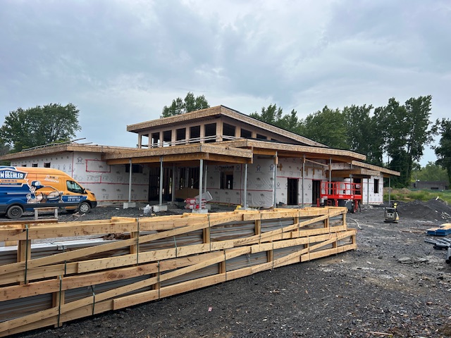 Building under construction with wooden frame structure, protective wrapping, and exterior walls in progress